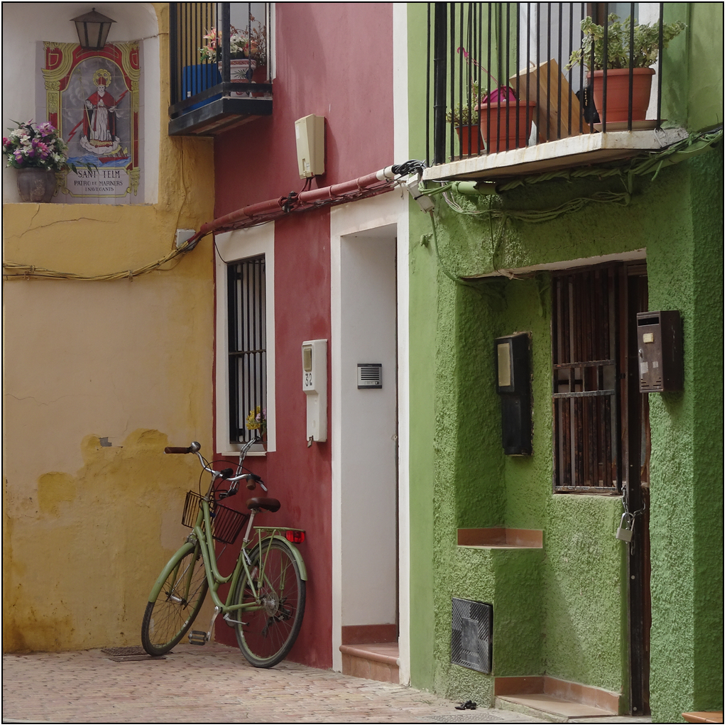 façades colorées, 1 verte, 1 ocre, 1 jaune. Un vélo vert est adossé à la façade ocre