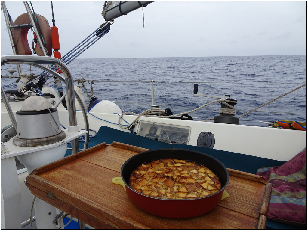 Cockpit de bateau en mer. Sur la table, un clafoutis aux pommes